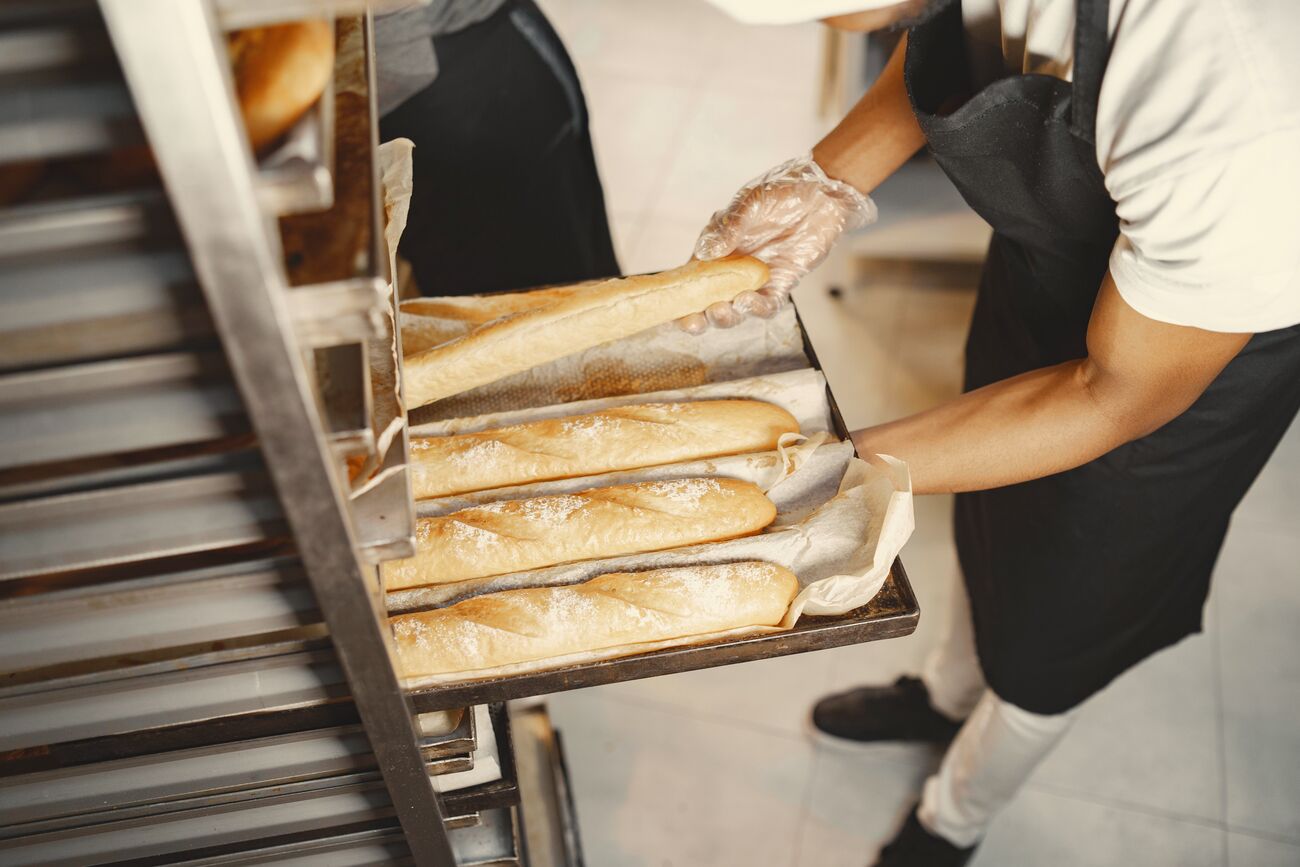 A baker sliding a tray of fresh baguettes onto a rack
