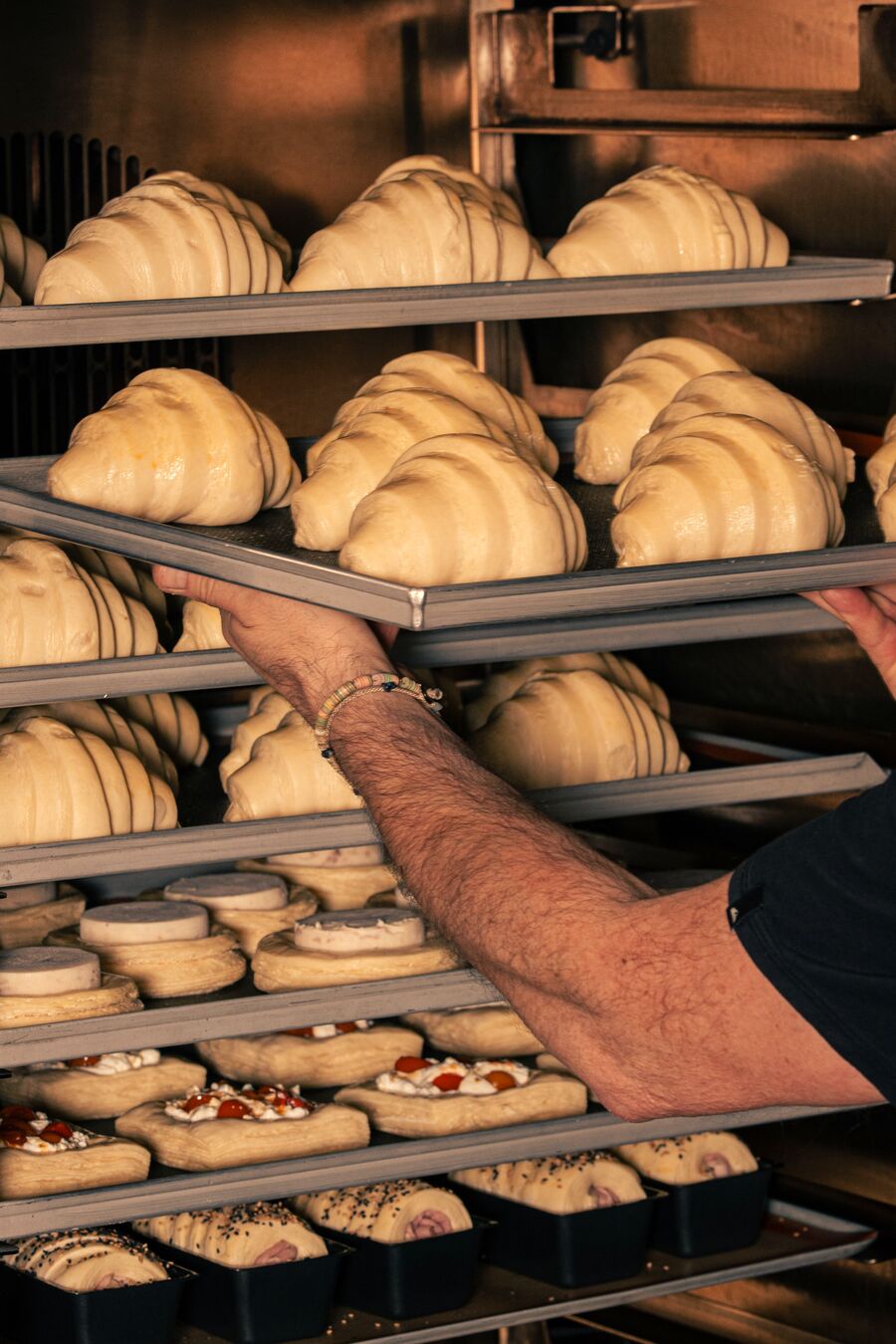 A baker sliding a tray of croissants onto a rack